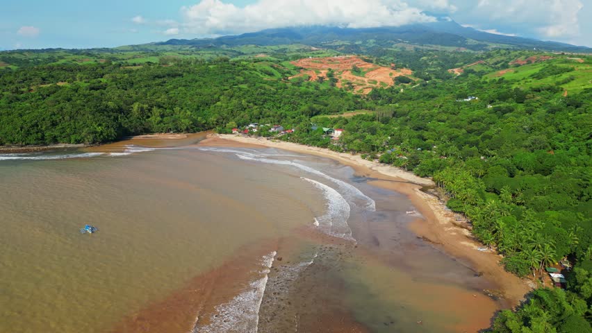 Raised aerial of Quinawan Beach in Mariveles, Bataan, capturing sandy shoreline, brown waters, and lush green hills framing the coastal village and palm‑lined edge.