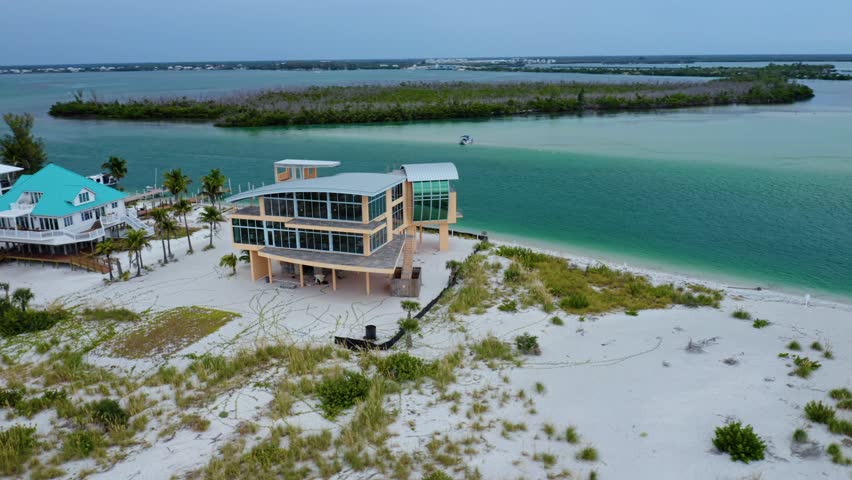 Elevated waterfront homes stand beside Stump Pass Channel on Florida’s Gulf Coast, surrounded by white sand, dune vegetation, and turquoise water facing the mangrove islands.