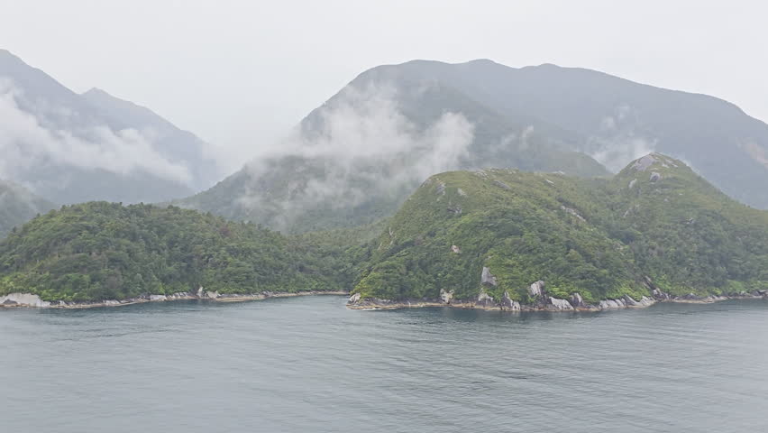 Milford Sound fiord presenting moody natural landscape with steep, forested mountains emerging through misty clouds, reflecting the dramatic and untouched wilderness of New Zealand