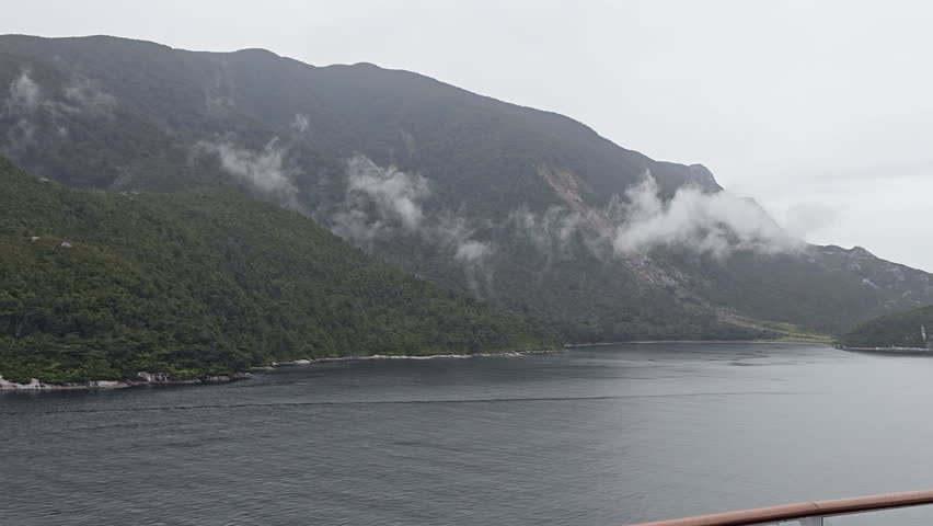 Milford Sound fiord showcasing misty mountain peaks and lush green slopes reflecting in calm water, creating serene natural landscape in Fiordland, New Zealand