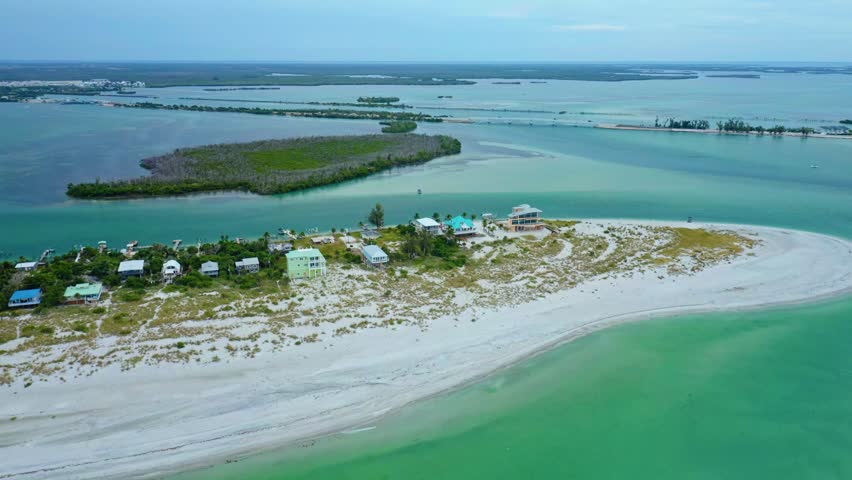 A sweeping sandbar peninsula arcs along Stump Pass beside waterfront homes on Manasota Key on Florida’s Gulf Coast, bordered by shallow turquoise water and distant mangrove islands across Lemon Bay.