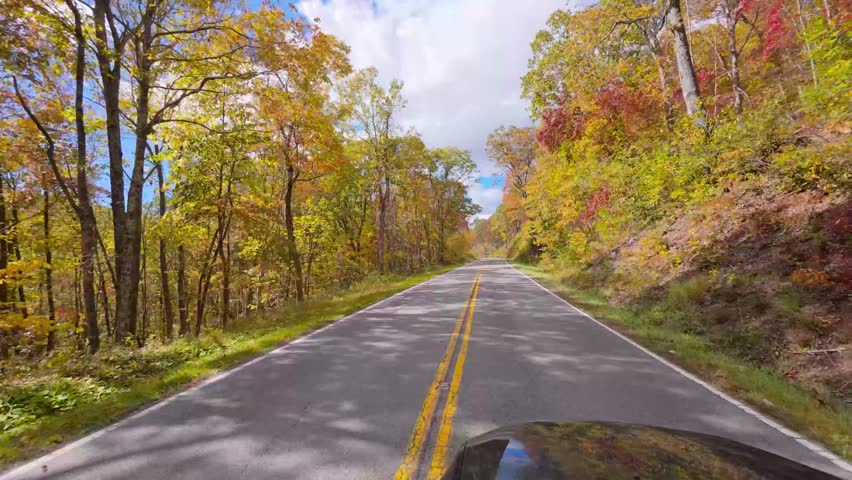 View from a car Driving along the Blue Ridge Parkway in autumn with colorful foliage lining the winding mountain road.