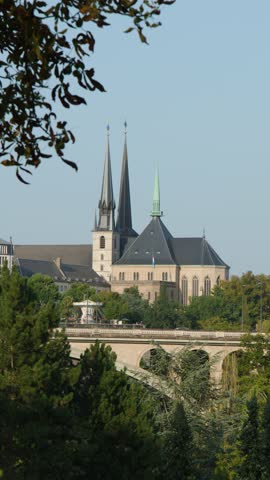 Cathedral spires and stone bridge framed by trees, daylight, static wide shot, clear sky