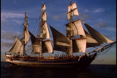 Historical reenactment of HMS Bounty ship on Rhode Island. MS side view of Bounty under full sail on very dark sea. Bright sunlight is hitting the side of the ship.