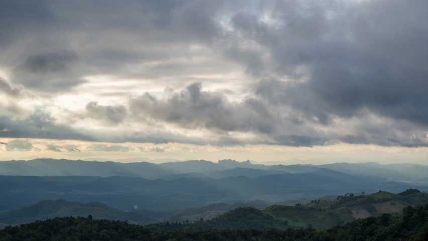 Breathtaking time-lapse capturing endless mountain ranges stretching across the horizon as the sun descends and clouds drift continuously overhead in Tak Province, Thailand. 