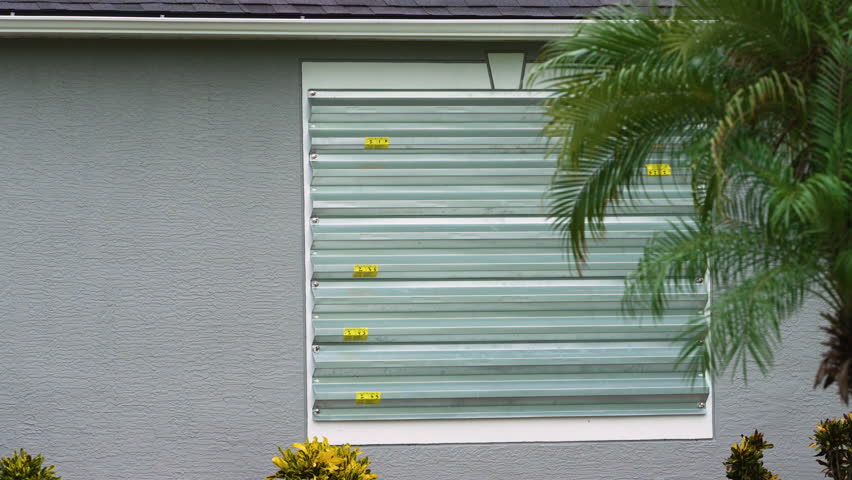 Storm resistant steel shutters cover windows of Florida house as precaution before hurricane. Home prepared for extreme weather