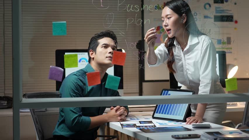 Asian business people working together on a business plan, using sticky notes on a glass board