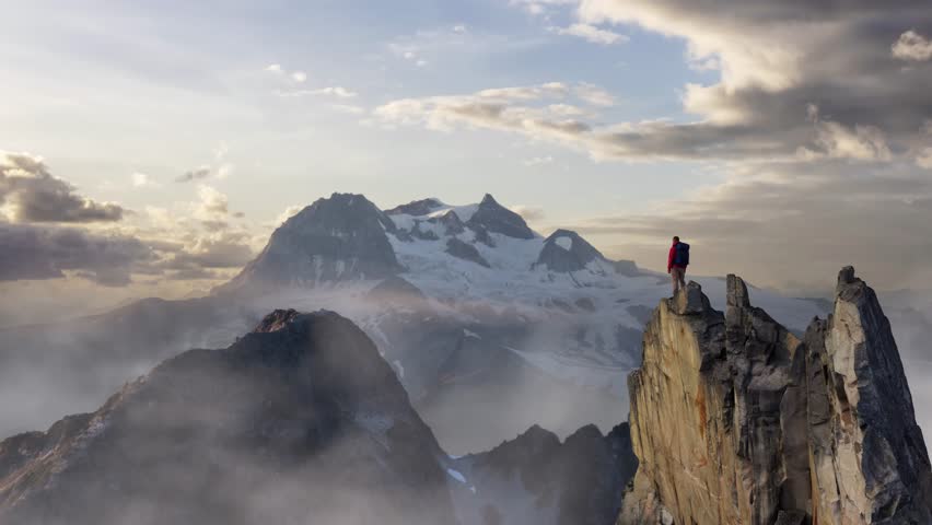 Hiker Standing Triumphantly on a Mountain Peak Overlooking a Majestic Snowy Landscape
