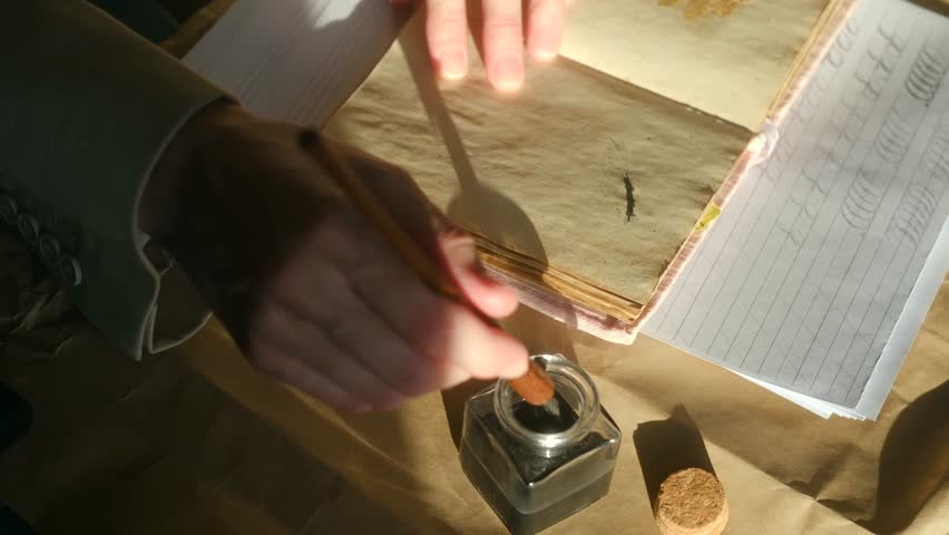 Close up calligrapher hands dipping classic nib pen into an inkwell and writing in vintage journal, practicing art beautiful handwriting on aged paper in sunlight. Practicing old calligraphy nib pen