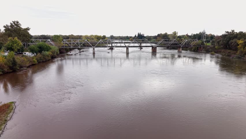From the air, the Tehama Railroad Bridge appears as a bold steel span cutting across the calm river, framed by the open landscapes surrounding Mill Creek Park.