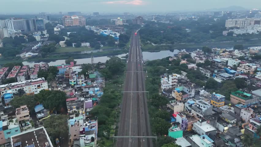 Aerial view of Chennai’s busy rail corridor running through packed residential blocks, over a major waterway, and toward corporate high-rises—highlighting vital urban connectivity.