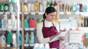 Saleswoman carefully counts the balance of goods and writes down in the documents that then replenish the stock of the warehouse. Supermarket worker conducts an inventory of household chemicals - Powered by Shutterstock - Get 15% off with code: PIKWIZARD15