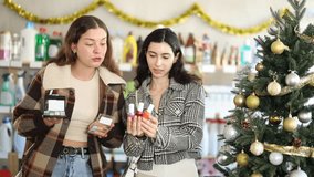 Women buy nail polishes and a set of makeup cosmetics against the background of a Christmas tree in the supermarket. Customers choose a set of cosmetics for festive New Year promotions and discounts - Powered by Shutterstock - Get 15% off with code: PIKWIZARD15