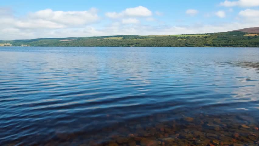 Low-angle panning shot of Loch Ness in Scotland, showcasing the vast deep freshwater loch, scenic highland surroundings, and serene waters.