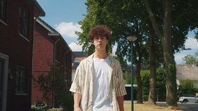 Young man checking phone on residential street midday with curly hair and relaxed posture, portrait framing shows buildings, trees and bright sky, candid content creation vibe, social - Powered by Shutterstock - Get 15% off with code: PIKWIZARD15