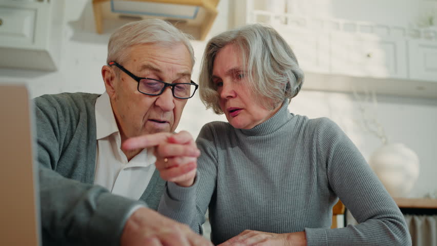 Frustrated old woman and husband viewing paper and looking for info in laptop. Senior people examining bank or medical papers, financial or health problems, family support, calm and emotional spouses