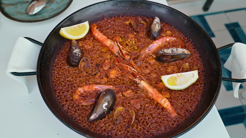 Traditional seafood paella served in a black paellera pan, garnished with lemon wedges, prawns, mussels and clams