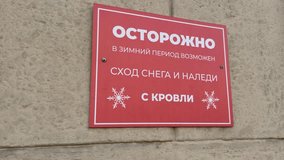 Red sign in Russian on wall of building warns of potential danger of snow and ice falling from roof during winter. Warning sign about snow and icicles falling from roof of building - Powered by Shutterstock - Get 15% off with code: PIKWIZARD15