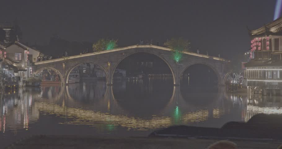 Zhujiajiao, Shanghai, China. exquisite scene features a lit stone bridge and riverside houses, with their reflections shimmering gracefully on the water, encapsulating nighttime tranquility and charm.