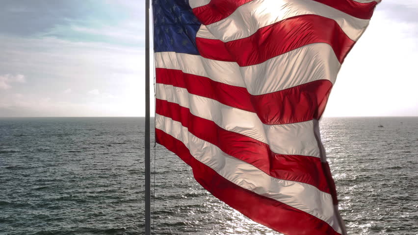 American flag in coastal wind. US flag over open water. Flag rippling in ocean air. American flag above water. - Powered by Shutterstock - Get 15% off with code: PIKWIZARD15