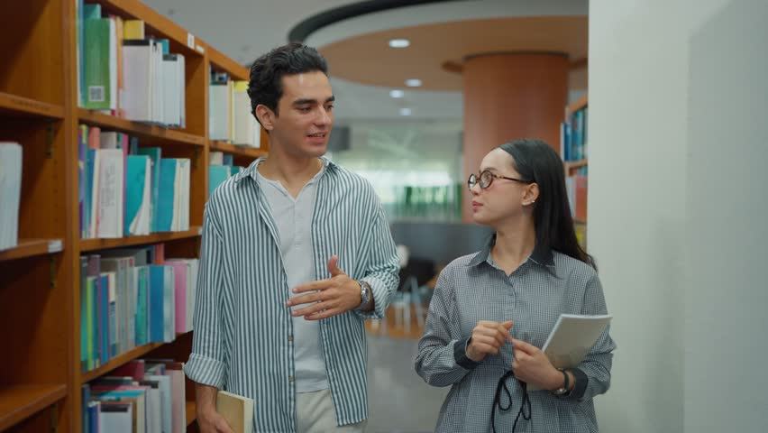 Male and female university friends walking and discussing while searching for research in the library. Collaborative study and learning concept