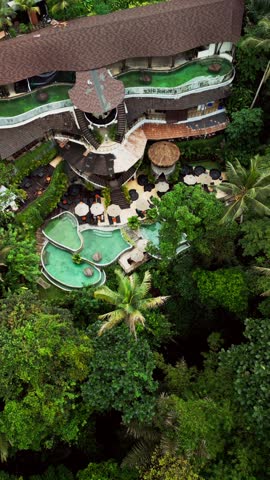 Vertical drone footage of a Bali jungle resort with tiered pools, shaded daybeds, and dense valley, providing a straightforward look at the tropical hillside layout and the natural forest environment