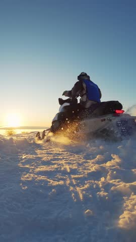 Lone snowmobile rider traverses through the serene snow-covered mountains at sunset