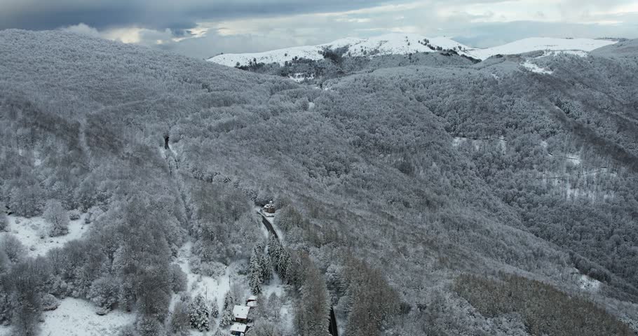 Aerial panoramic view of snow covered mountain range landscape under cloudy winter skies