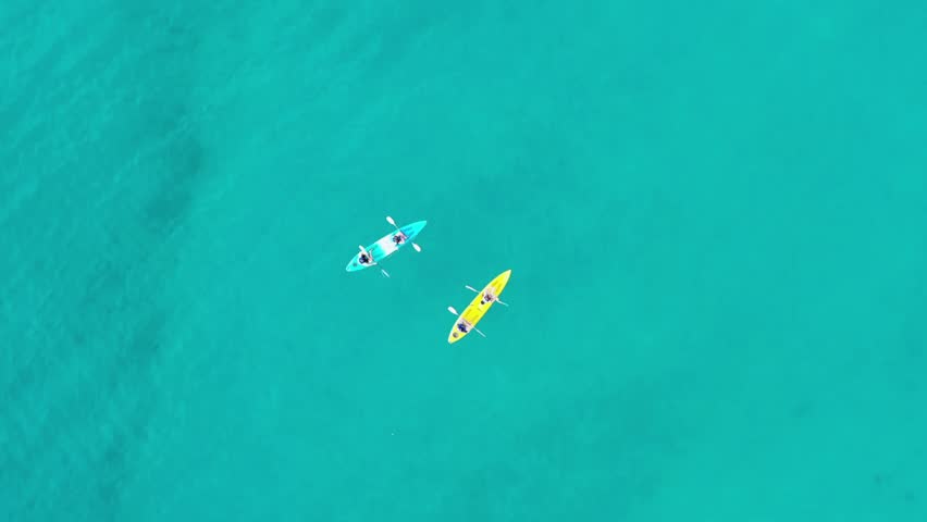 Aerial view of two kayaks paddling in crystal clear turquoise ocean water today