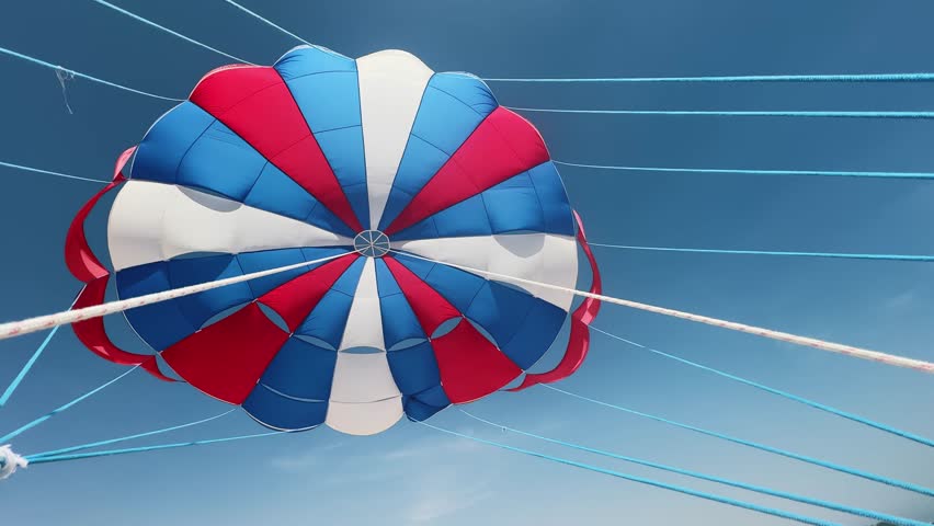 Flying pov with colorful parasailing chute suspended in blue skies over a serene summer beach