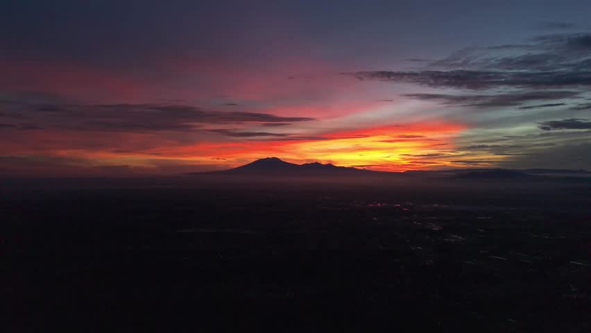 Aerial view of a mountain silhouette against a vibrant sunrise, with shades of red, orange, and purple blending seamlessly, Klaten Regency, Central Java, indonesia.