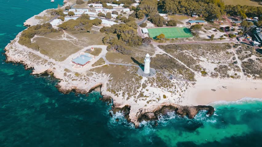Cinematic aerial footage panning around the Bathurst Lighthouse on Rottnest Island. The lighthouse is surrounded by sandy white beaches and the turquoise blue ocean.