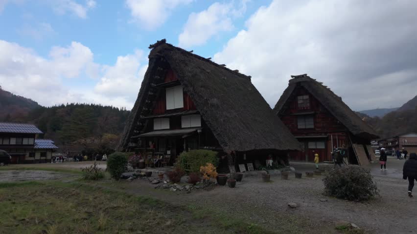 Traditional thatched house in a rural Japanese village with mountain scenery.