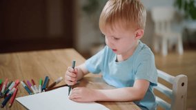 Boy in blue shirt holding marker drawing on white paper surrounded by colorful pens at wooden table with woman nearby, showing focus, learning, childhood creativity, education, imagination, artistic - Powered by Shutterstock - Get 15% off with code: PIKWIZARD15