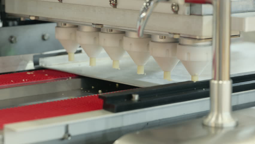 Automated pastry machine forming dough on a tray in a confectionery factory. Precision nozzles create uniform pastries on a production line, representing modern food manufacturing.