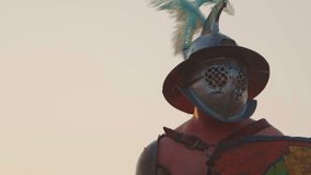 A cinematic, dramatic close-up of a Roman gladiator in detailed armor and crested helmet (galea), slowly raising a curved sword (sica) with a focused, intense action shot against a hazy sky. - Powered by Shutterstock - Get 15% off with code: PIKWIZARD15