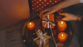 A detailed 4K view of a person's hands wrapping Christmas gifts, including an orange box, illuminated in a cozy candlelight scene. - Powered by Shutterstock - Get 15% off with code: PIKWIZARD15