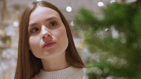 Close-up of young woman admiring beautifully hanging tinsel in a festive store, she is surrounded by holiday decorations, including garlands and shimmering lights in a seasonal shopping mall - Powered by Shutterstock - Get 15% off with code: PIKWIZARD15