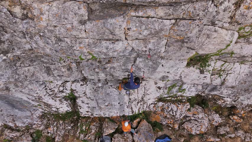 Lead Climbing and Belaying. Rock Climber on Overhanging Crag Clipping Quickdraws and Climbing Higher. Aerial Drone Shot