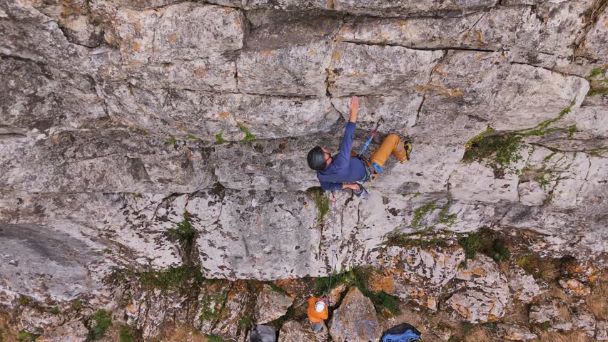 Lead Climbing and Belaying. Rock Climber on Overhanging Crag Clipping Quickdraws and Climbing Higher. Aerial Drone Shot