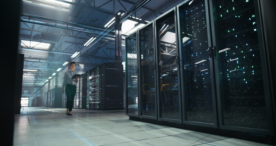 Asian and White It Engineers Walk Through a Vast Data Center, Analyzing Holographic Dashboards on Server Racks, Tracking Cloud Capacity, Managing Infrastructure, Secure Data Operations on Tablets.