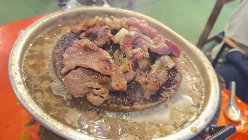 Sizzling meat on hot plate creates delicious aroma and appetizing scene, showcasing savory cuts of beef and pork cooking in flavorful juices for unforgettable dining experience at restaurant