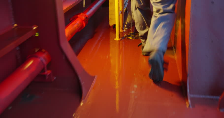 Crew member in helmet walks calmly across steel deck. Sunlight glints from metal surface blending warmth and control. Teamwork on ship