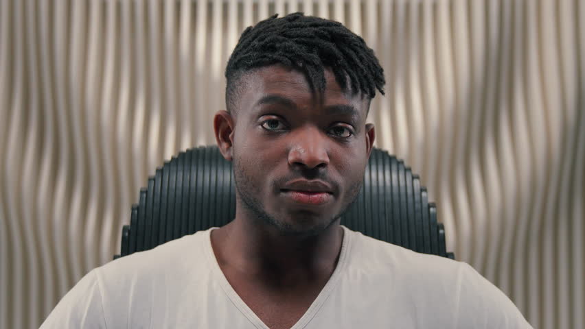 Stylish fashionable serious African American man putting on glasses in white futurism studio futuristic modern male guy put on sunglasses fashion style posing sit in chair innovative technology space