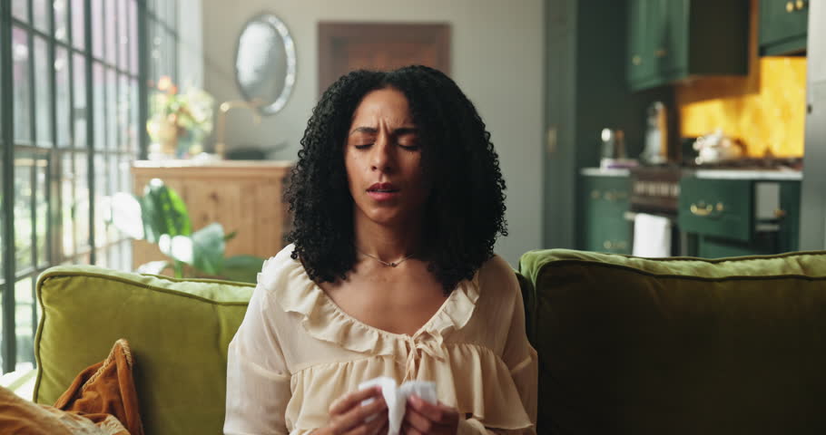 Woman, sneeze or blowing nose on couch with tissue for influenza, health problem and virus symptoms. Sick person, allergies or illness in home with toilet paper for hayfever, cold or sinus infection.