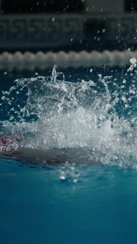 Dramatic close up of splashing water as a swimmer powers through a blue indoor pool lane, capturing dynamic motion, droplets, and athletic intensity