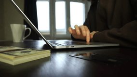 A man focuses on a laptop, tapping keys as he holds a credit card. Nearby, cash is stacked beside the laptop on the desk, highlighting the laptop's role in transactions. - Powered by Shutterstock - Get 15% off with code: PIKWIZARD15