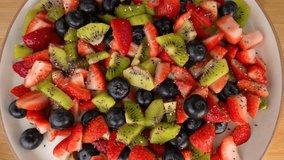 A top view of a colorful fruit salad with sliced strawberries, kiwi, and blueberries, sprinkled with chia seeds, on a white plate - Powered by Shutterstock - Get 15% off with code: PIKWIZARD15