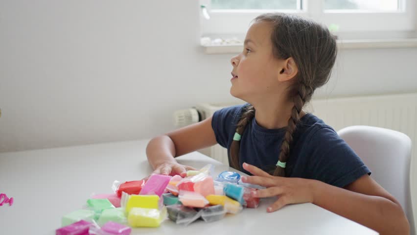 young caucasian girl meticulously arranging colored clay sets in sunlight, an impression of young white girl arranging pastelcolored modeling clay packs by sunny window with thoughtful focus
