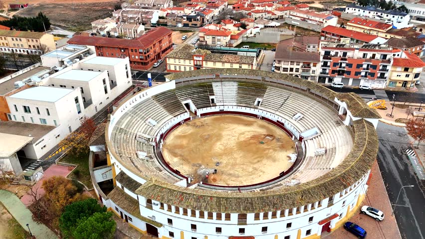 Bullring in Tarazona de la Mancha, Albacete, Spain, highlighting the circular architecture, tiled plaza, and surrounding residential buildings under overcast light.
